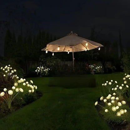 Garden with a lit outdoor umbrella and decorative string lights on plants at night.