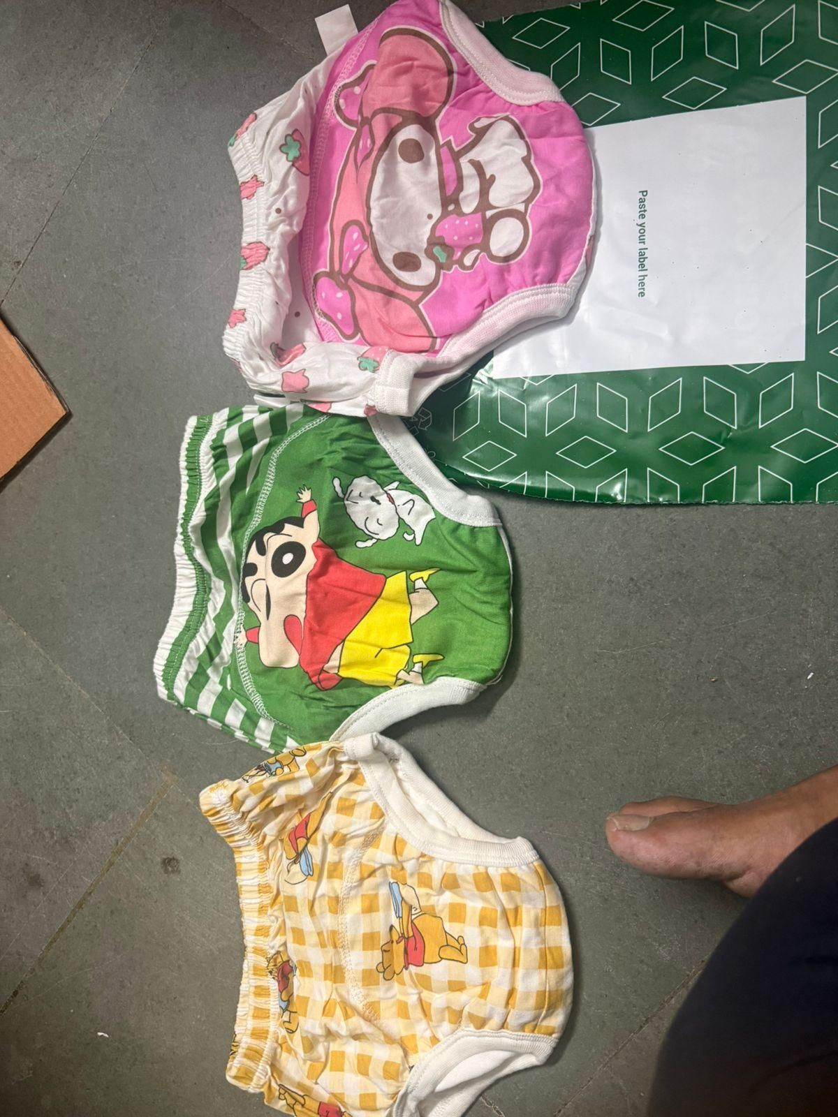 Three children's underwear with cartoon designs on a gray floor.
