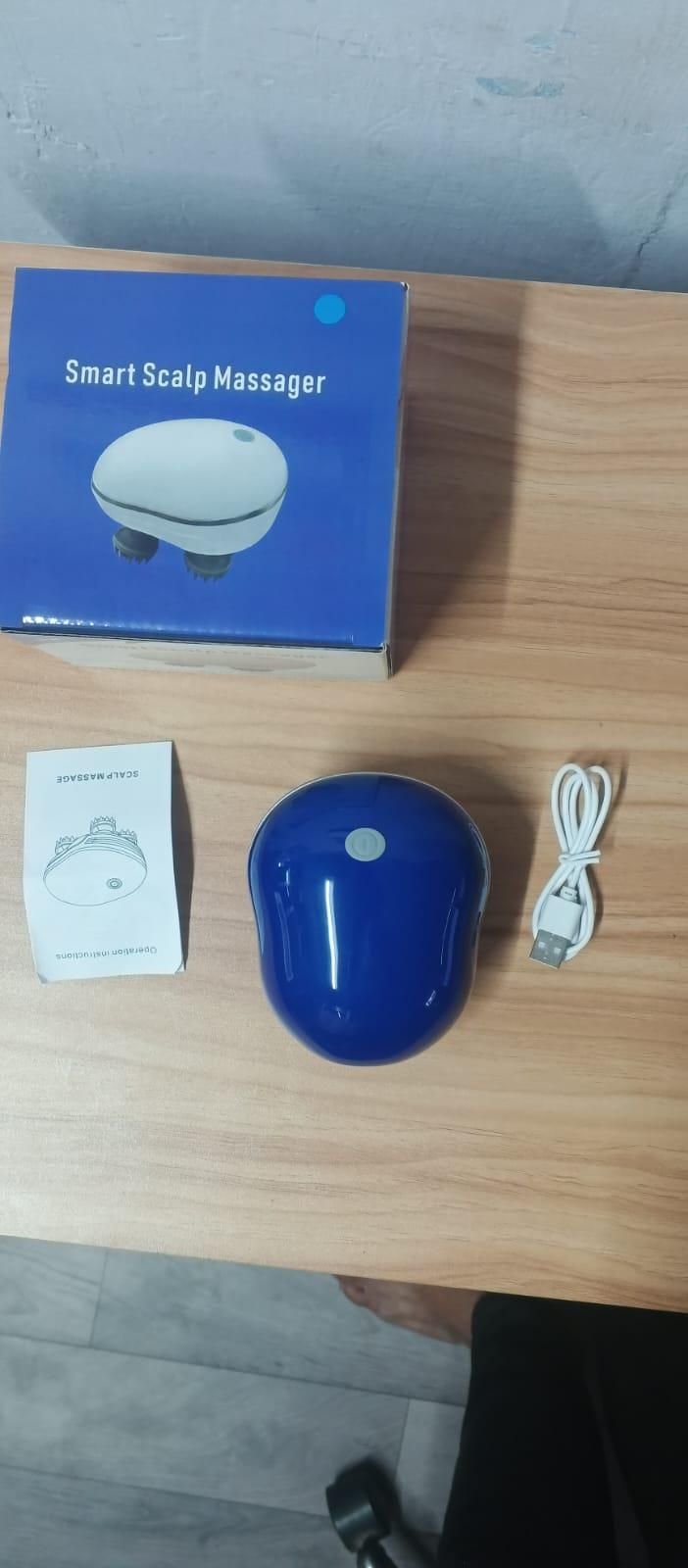 Smart scalp massager with packaging, user manual, and USB cable on a wooden surface.