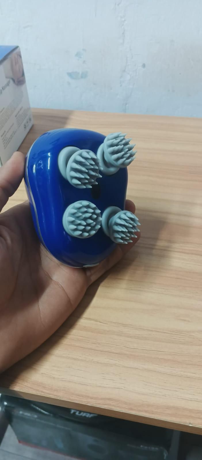 Blue handheld device with textured nodes held by a hand on a wooden surface.