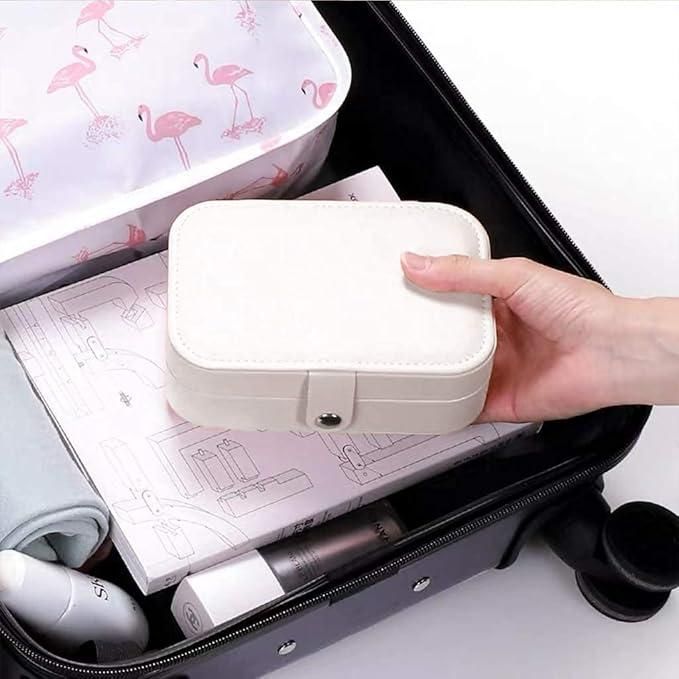 Hand holding a small white suitcase over an open suitcase with travel items on a white background